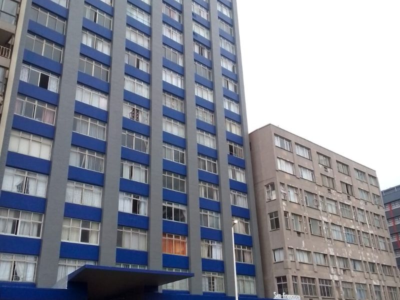 Street view of a multi-story apartment building featuring a blue and grey facade with ground floor commercial retail spaces.