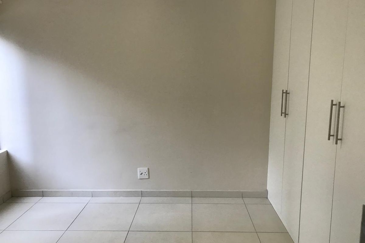 A clean, empty bedroom featuring neutral tiled flooring and white built-in cupboards, providing a blank canvas for personalization.