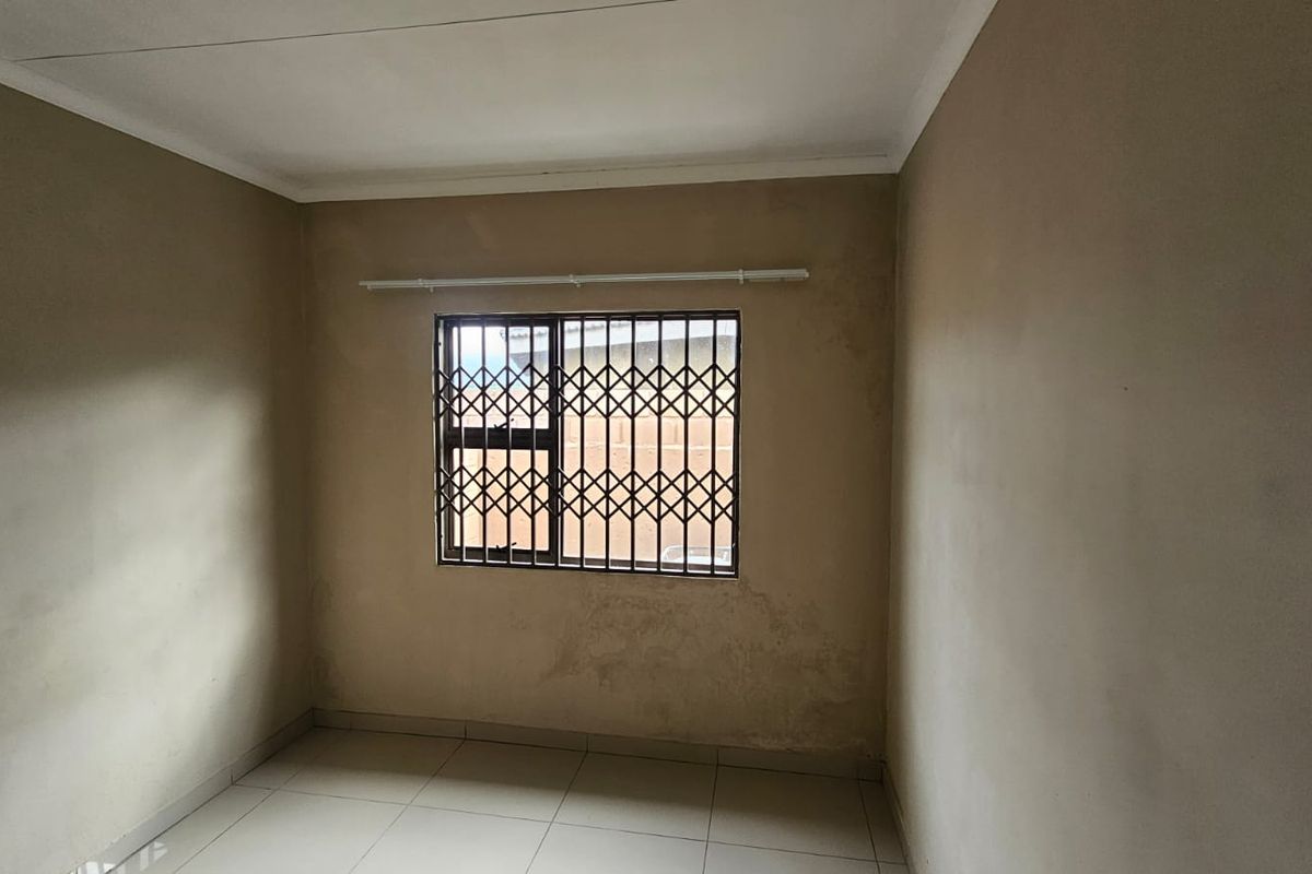 An empty bedroom featuring tiled flooring, a window with security bars, and plain wall finishes, offering a blank canvas for renovation.