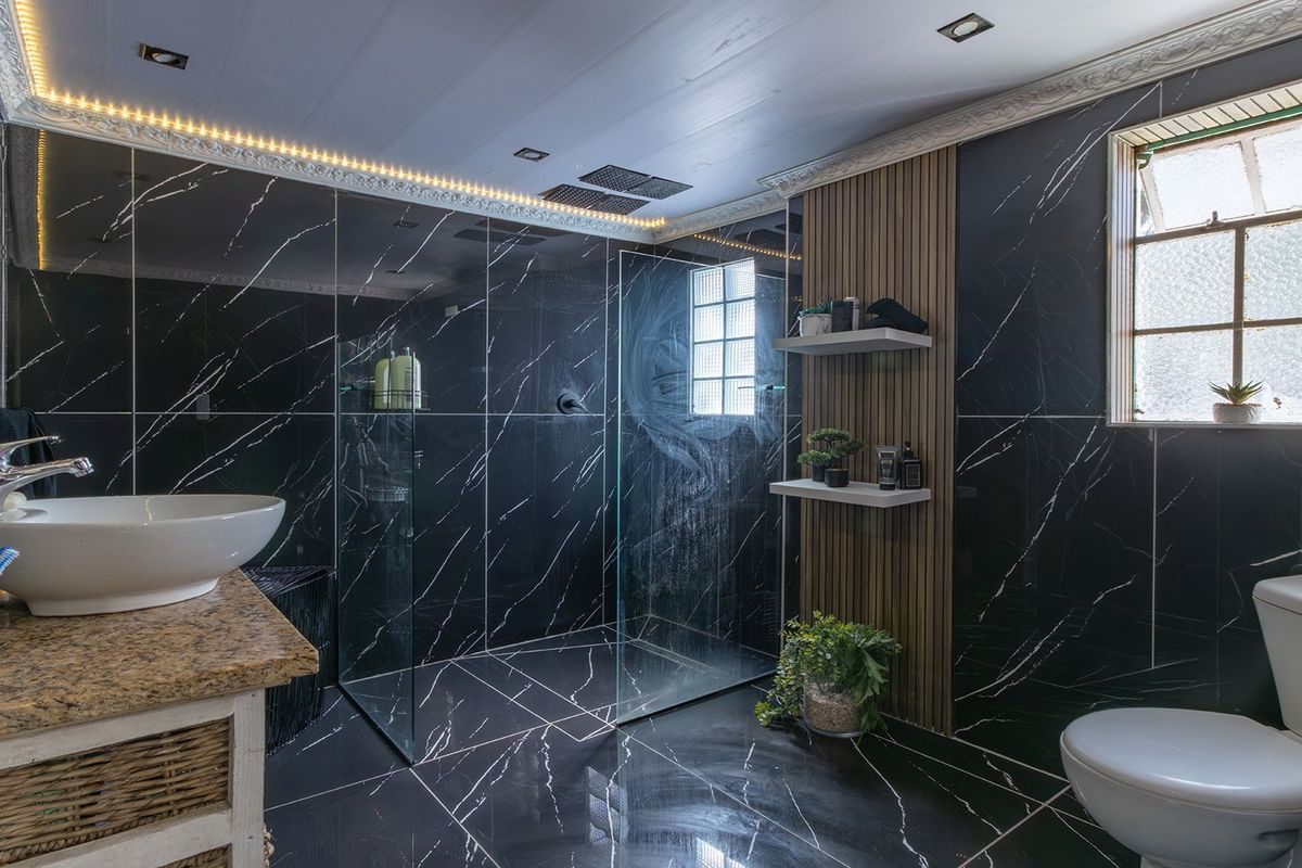 Modern bathroom featuring black marble-look wall and floor tiles, a vessel sink on a granite vanity, and a spacious walk-in shower with glass enclosure.