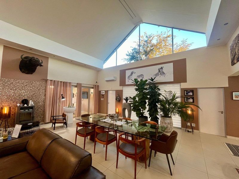 Spacious open-plan living and dining area featuring a dramatic vaulted ceiling, large triangular clerestory windows, and a modern fireplace with a mosaic feature wall.
