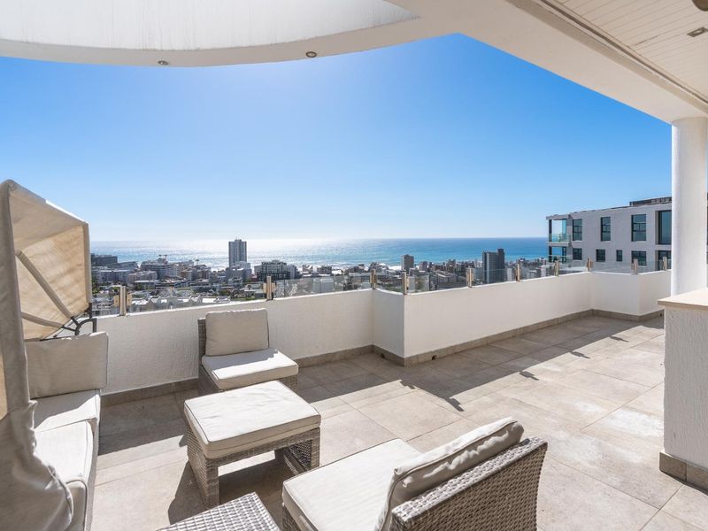 Spacious covered balcony featuring tiled flooring, a modern glass balustrade, and panoramic coastal city views.