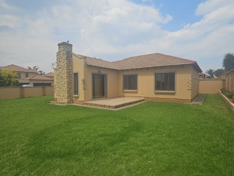 Rear view of the townhouse featuring a stone-clad chimney, tiled roof, paved patio area, and a spacious private garden.