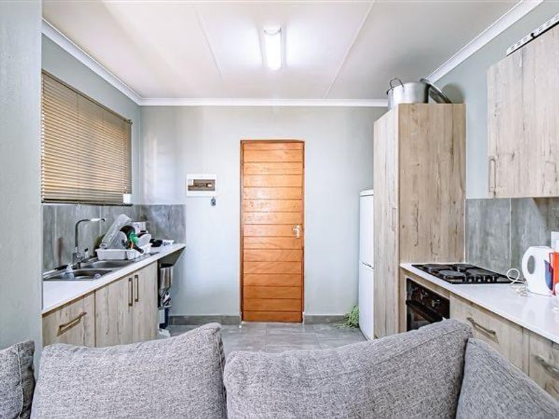A functional kitchen featuring light wood-look cabinetry, a built-in oven and hob, stainless steel sink, and tiled splashbacks with neutral wall finishes.