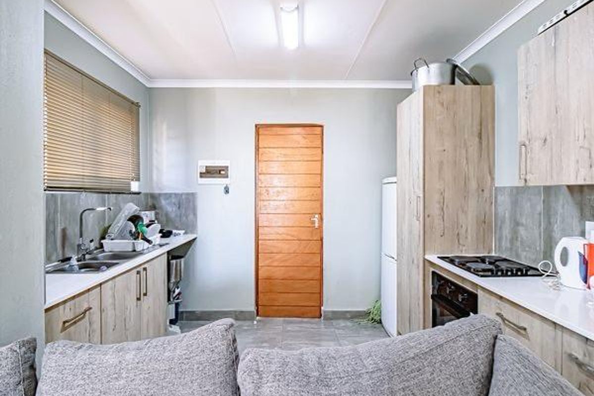 A functional kitchen featuring light wood-look cabinetry, a built-in oven and hob, stainless steel sink, and tiled splashbacks with neutral wall finishes.