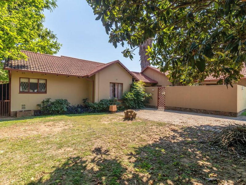 Rear view of the house featuring a tiled roof, paved driveway, and a spacious garden area with boundary walling.