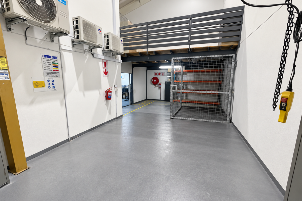 A clean, well-maintained industrial utility space featuring epoxy flooring, a mezzanine level with safety railing, security cage, and wall-mounted air conditioning units.