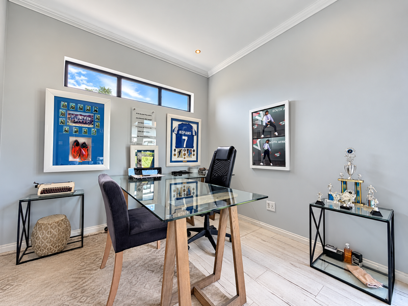A well-maintained home office featuring light-toned tiled flooring, crisp grey walls, and a horizontal clerestory window providing natural light.
