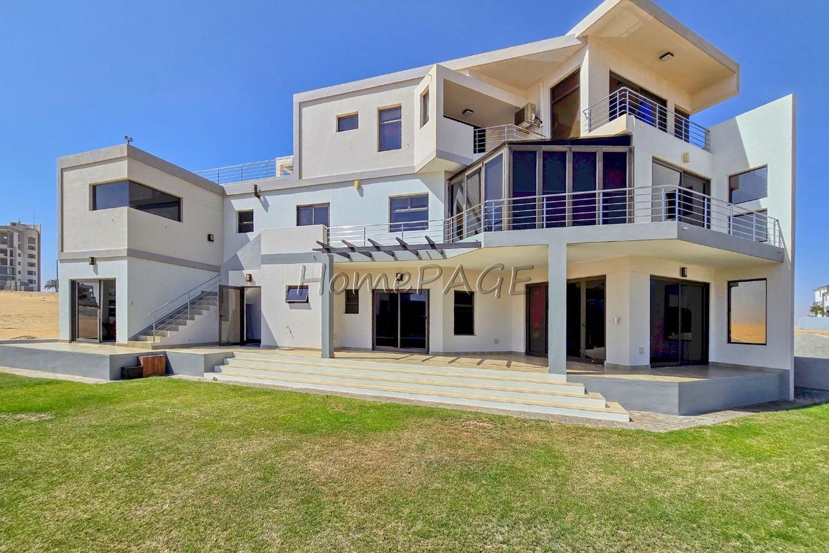 A modern multi-level residential property featuring expansive balconies, large glass sliding doors, and a spacious rear lawn area.