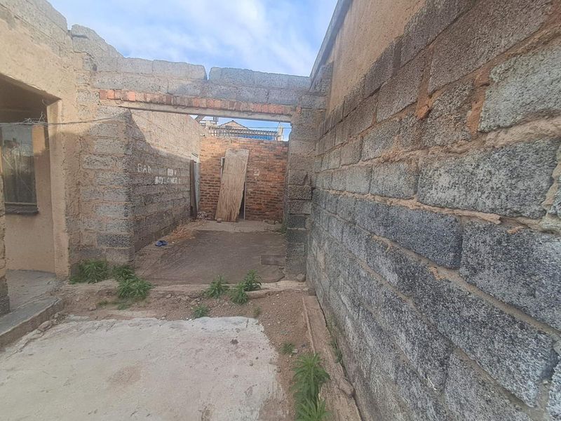An unfinished outdoor area featuring exposed concrete block walls and a concrete slab, currently in a state of construction or significant disrepair.