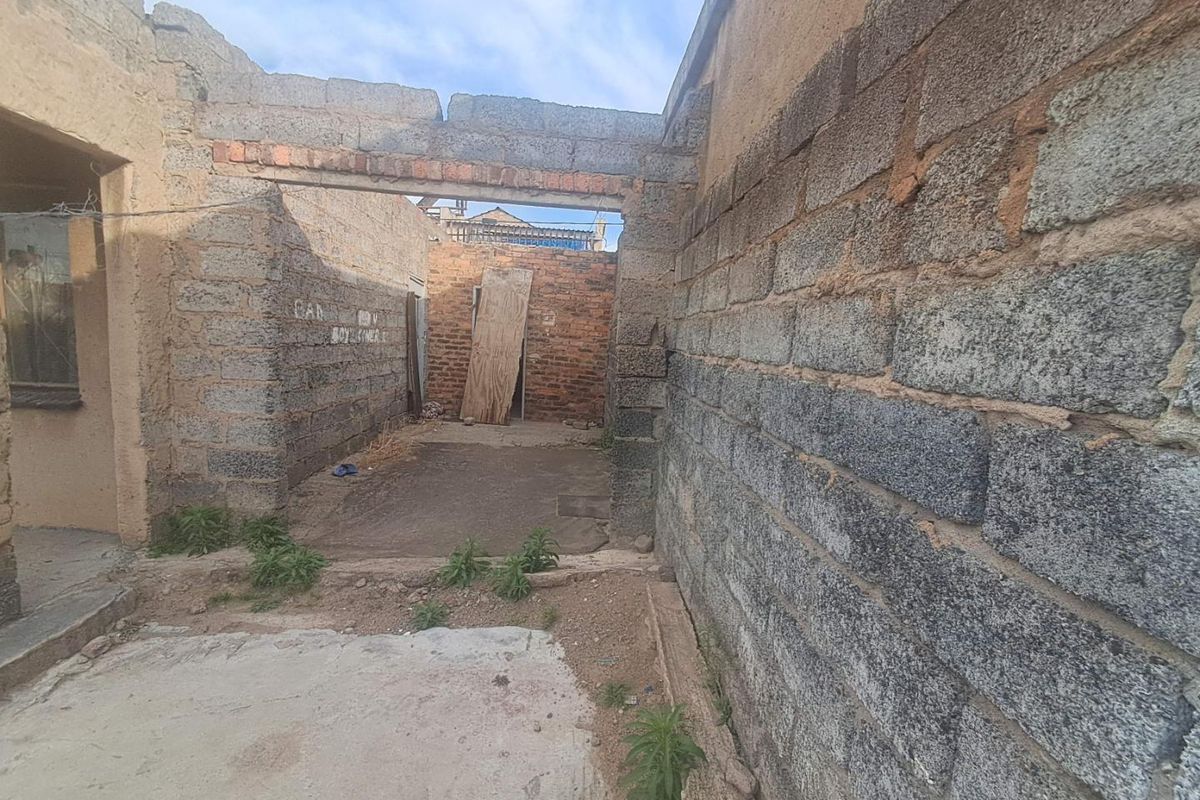 An unfinished outdoor area featuring exposed concrete block walls and a concrete slab, currently in a state of construction or significant disrepair.