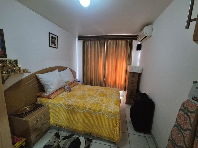 A compact bedroom featuring tiled flooring and a wall-mounted air conditioning unit, providing a functional space with natural light through window curtains.