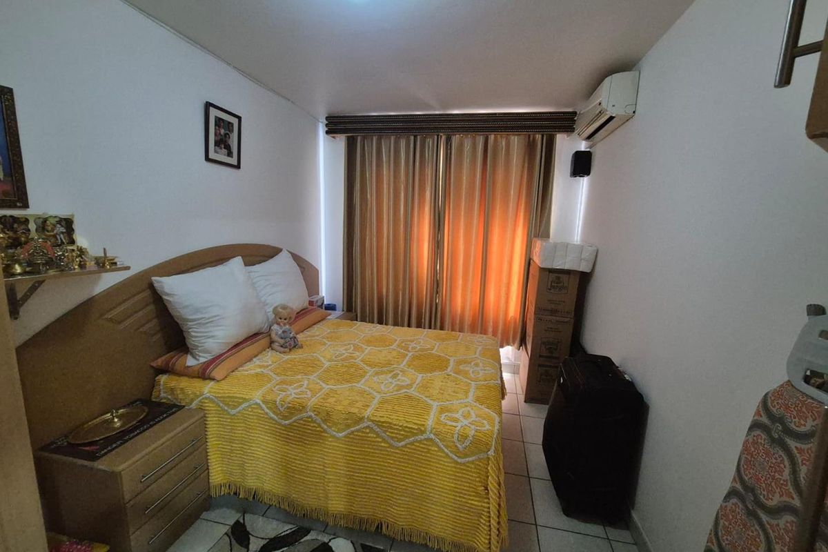 A compact bedroom featuring tiled flooring and a wall-mounted air conditioning unit, providing a functional space with natural light through window curtains.
