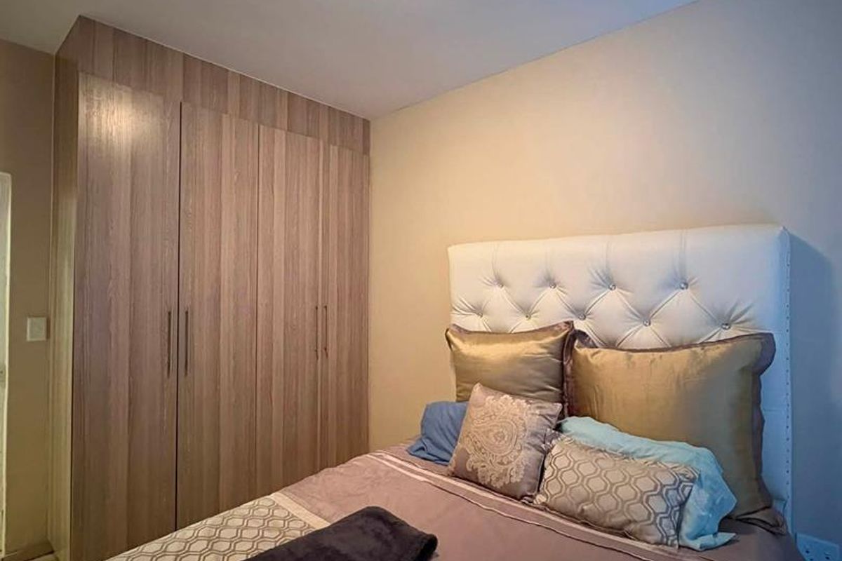 A well-maintained bedroom featuring modern wood-finish built-in cupboards and a central flush mount ceiling light fixture.