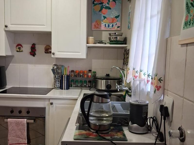 A compact kitchen featuring white cabinetry, a built-in oven with electric hob, tiled backsplash, and a stainless steel sink.