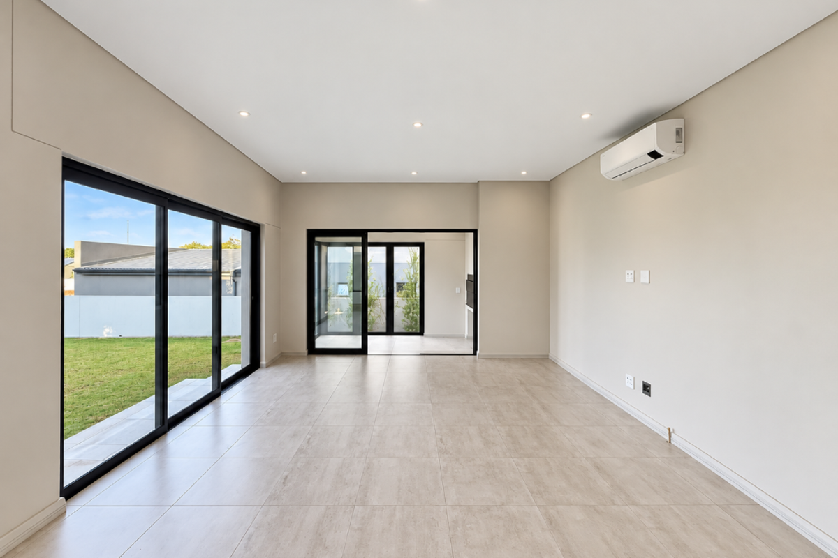 A bright, modern, and empty living area featuring large sliding glass doors, neutral tiled flooring, recessed lighting, and a wall-mounted air conditioning unit.