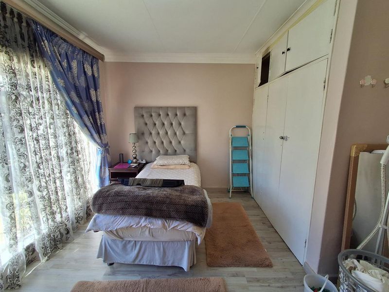 A bedroom featuring laminate flooring, built-in cupboards with overhead storage, and a large window with curtains.