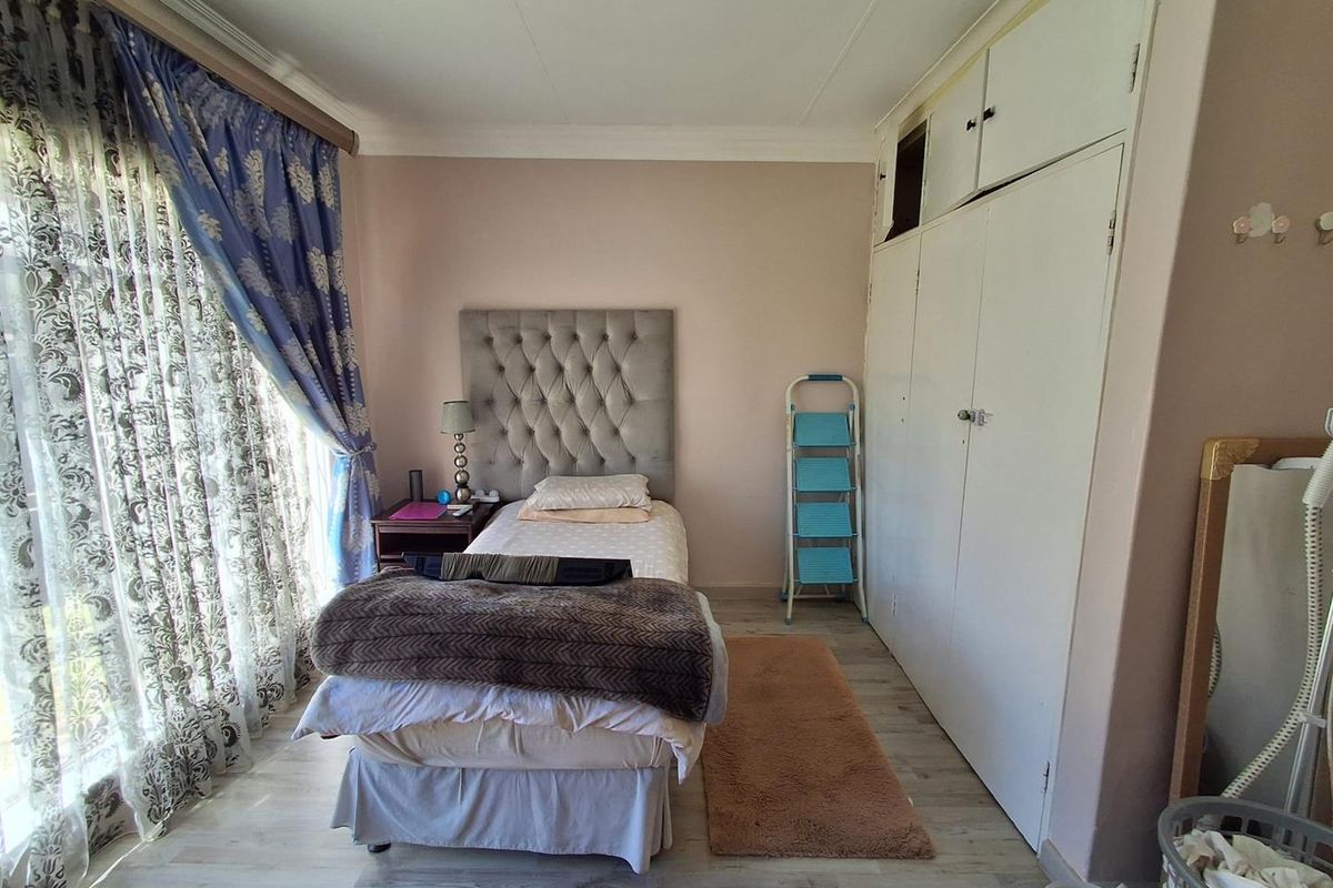 A bedroom featuring laminate flooring, built-in cupboards with overhead storage, and a large window with curtains.