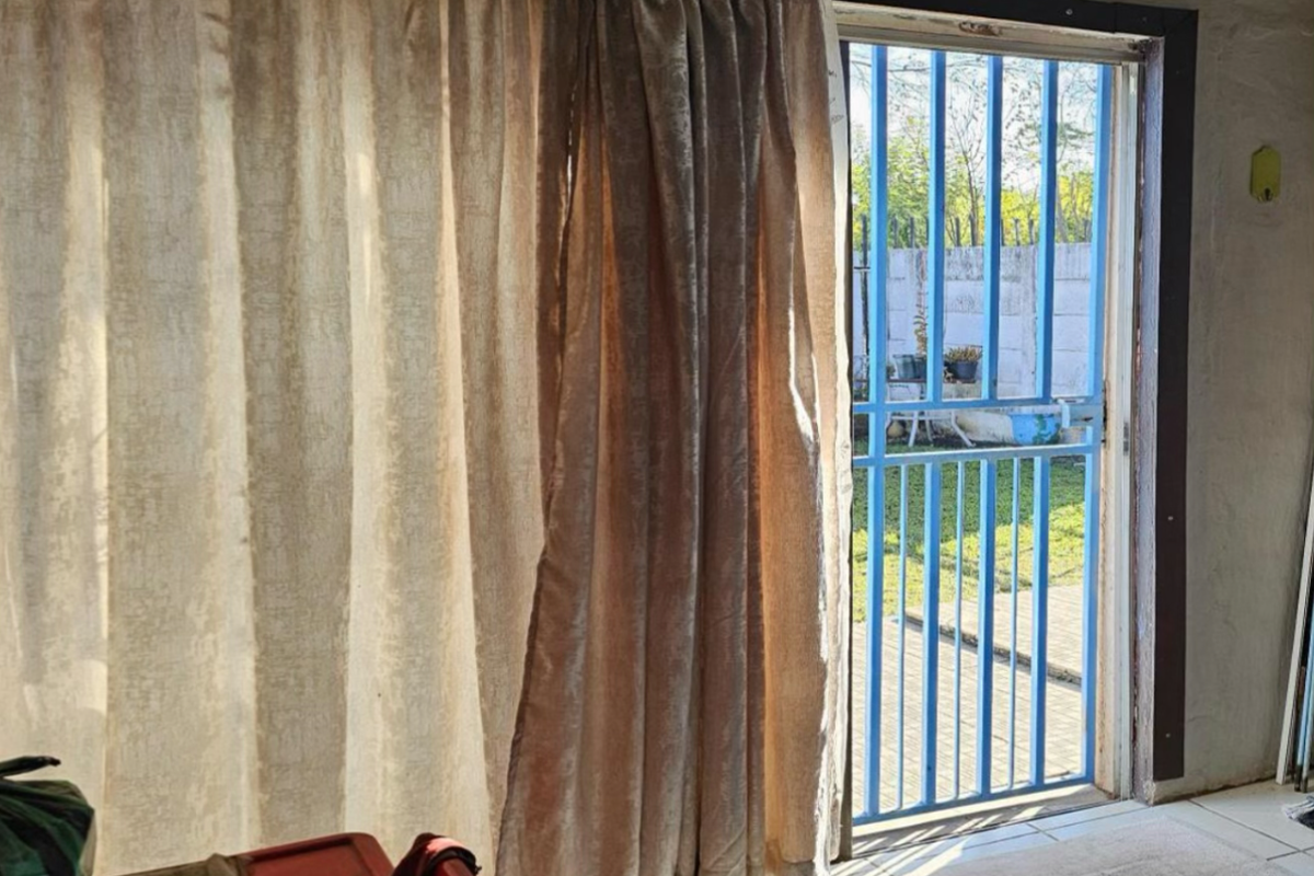 A living area featuring tiled flooring and a sliding door with a security gate, providing direct access to the outdoor space.