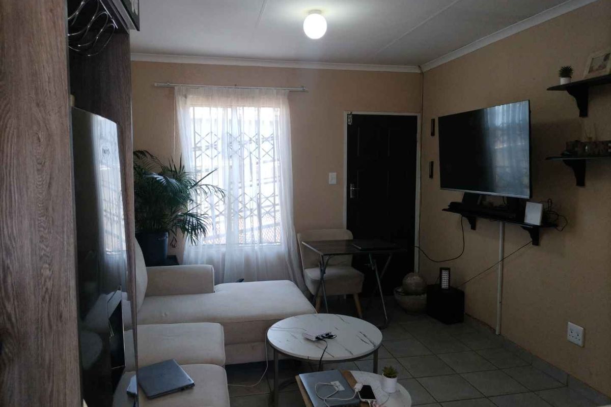 A compact living room featuring tiled flooring, a window with security bars, and a neutral wall finish.