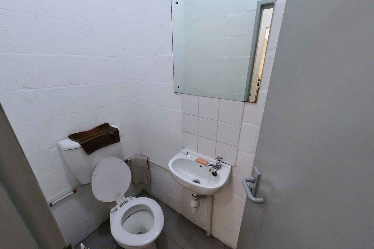 A compact industrial-style bathroom featuring a wall-mounted basin, toilet, and mirror with exposed brickwork walls.
