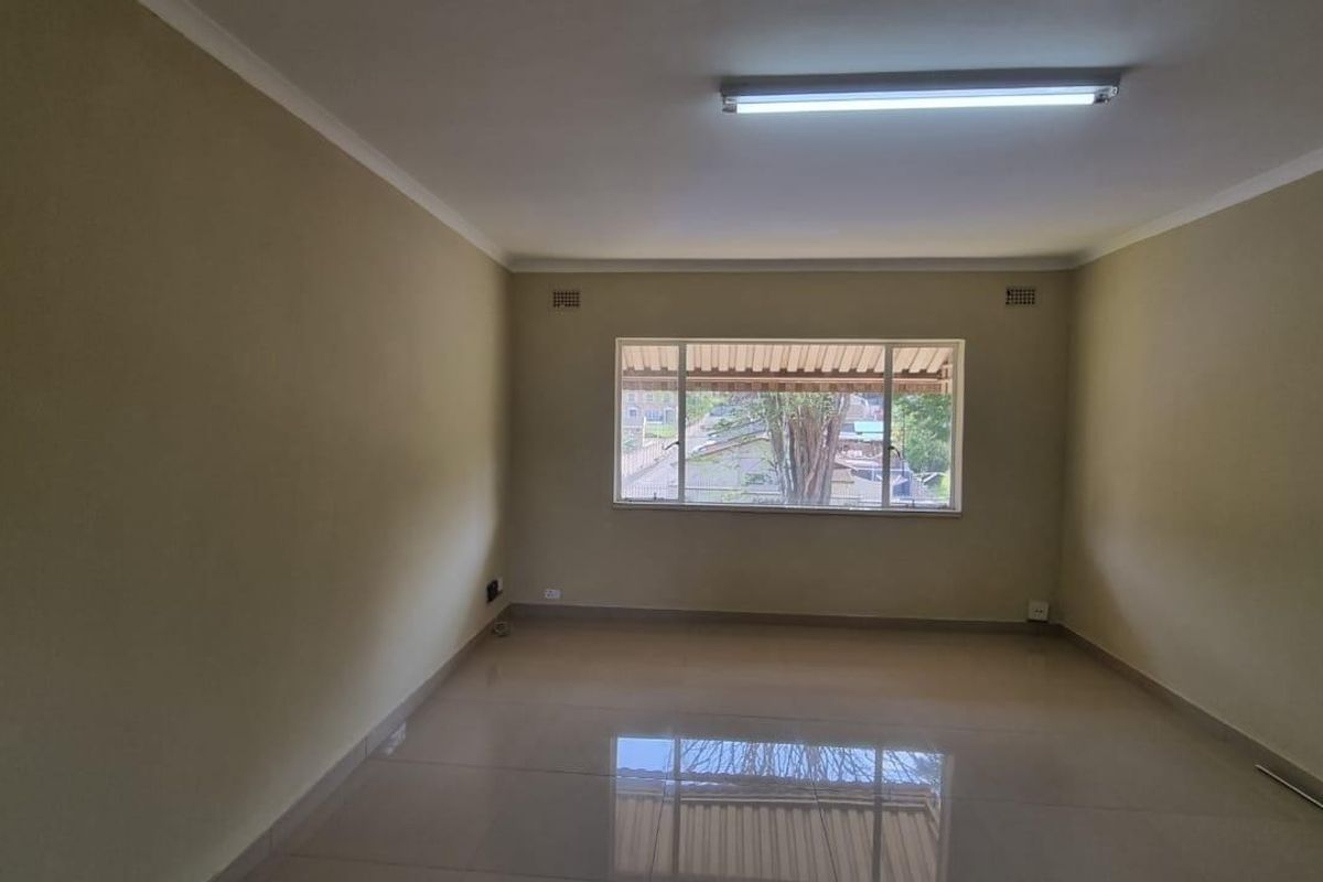 A spacious, empty living room featuring neutral walls, tiled flooring, and a large window providing natural light.