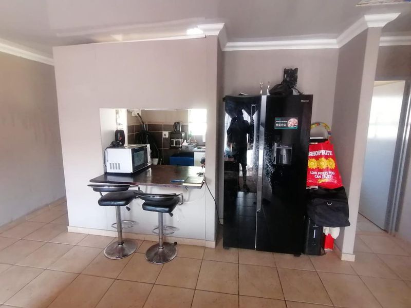 Open plan living area featuring a breakfast bar with a pass-through window connecting to the kitchen, finished with neutral wall paint and tiled flooring.