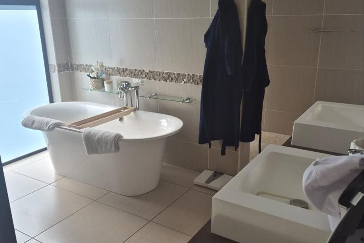 Modern bathroom featuring a freestanding bathtub, dual vanity basins with stone countertops, and neutral floor-to-ceiling wall tiles.