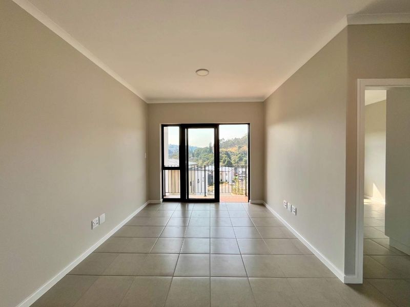 A bright, empty living room featuring neutral tiled flooring, clean walls, and a sliding glass door leading to an outdoor balcony area.