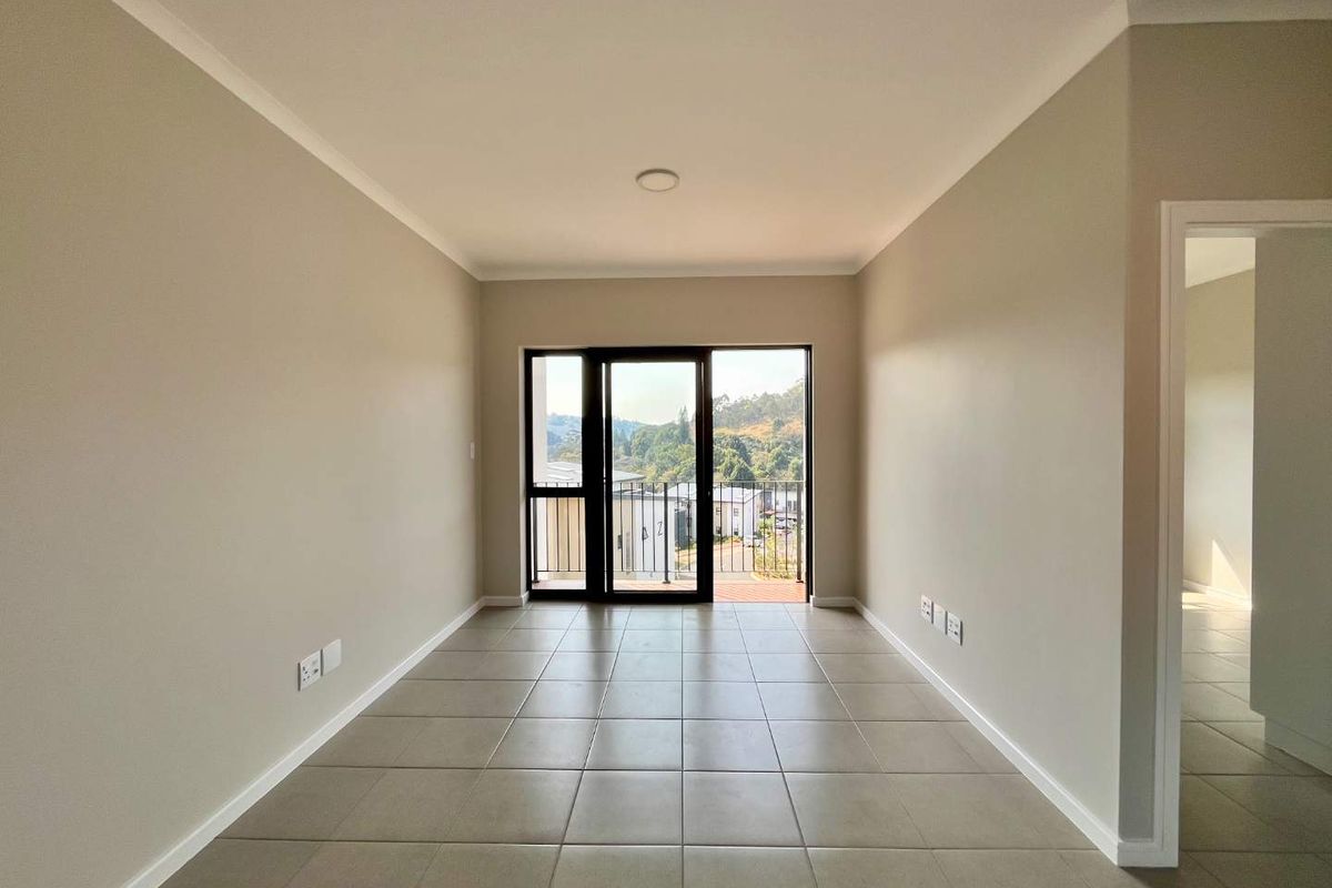 A bright, empty living room featuring neutral tiled flooring, clean walls, and a sliding glass door leading to an outdoor balcony area.