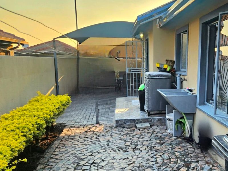 Rear exterior area featuring cobblestone paving, a shade sail, and a built-in utility sink against the house wall.