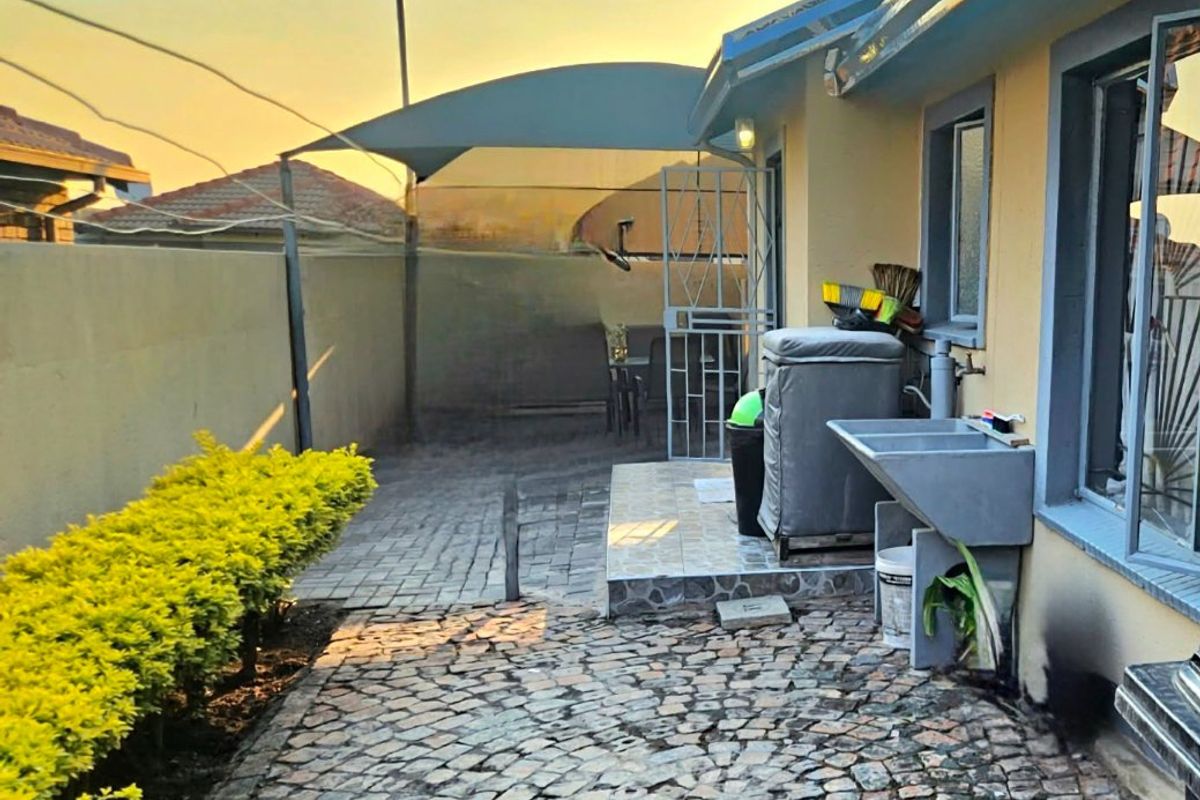 Rear exterior area featuring cobblestone paving, a shade sail, and a built-in utility sink against the house wall.