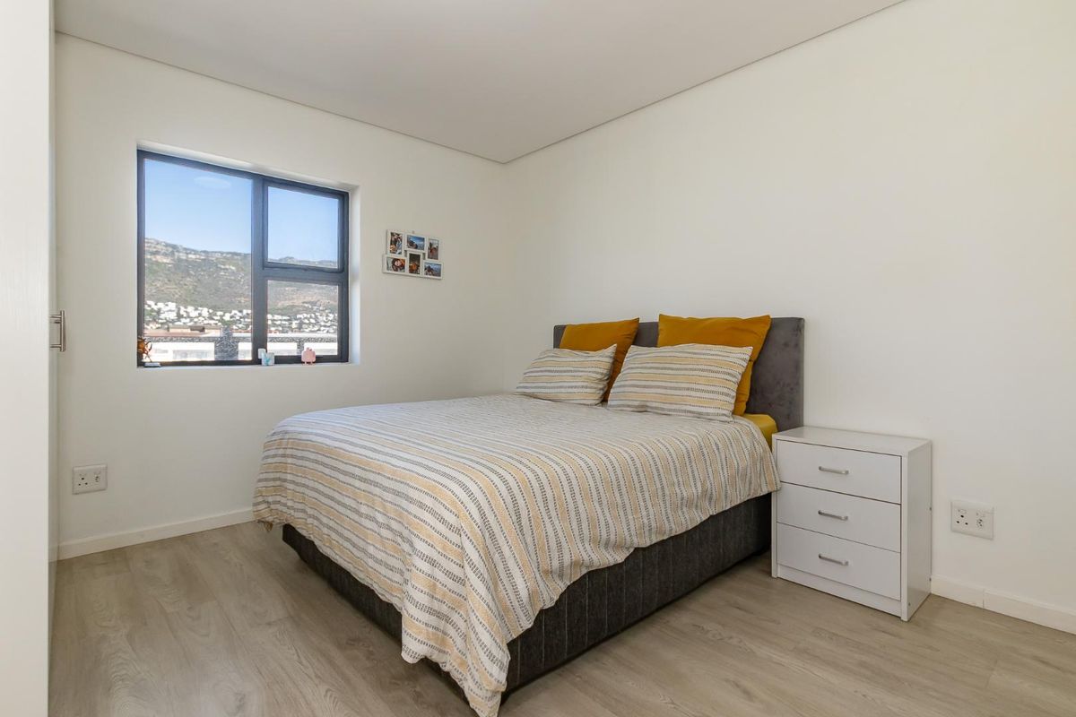A bright and modern bedroom featuring light wood-look flooring, neutral walls, and a window offering scenic mountain views.