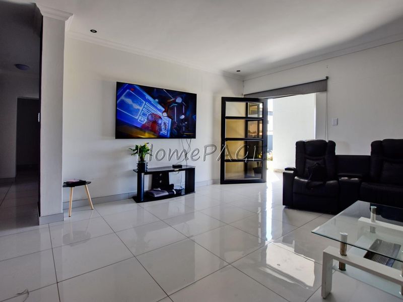 A bright living room featuring polished tiled flooring, recessed downlighting, and a glass-paneled door leading to an outdoor area.