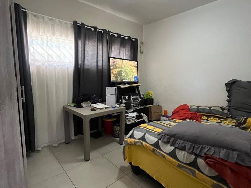 A functional bedroom featuring tiled flooring, a window with security bars, and a central ceiling light fixture.