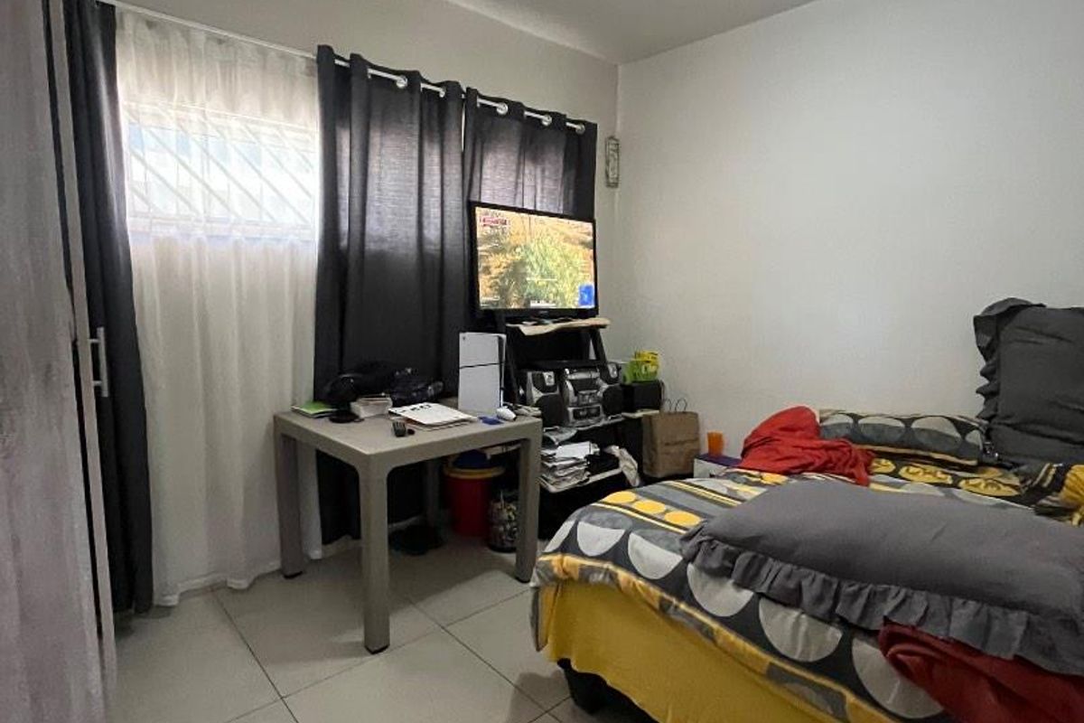 A functional bedroom featuring tiled flooring, a window with security bars, and a central ceiling light fixture.