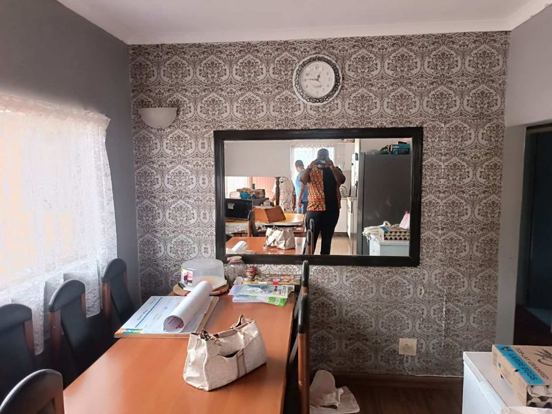 Dining area featuring patterned wallpaper, a large wall-mounted mirror, and laminate flooring. The space requires cosmetic updates to improve its overall condition.