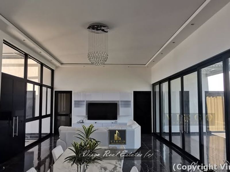 Modern living room featuring high ceilings, recessed lighting, a crystal chandelier, and expansive black-framed glass sliding doors opening to the outdoor area.