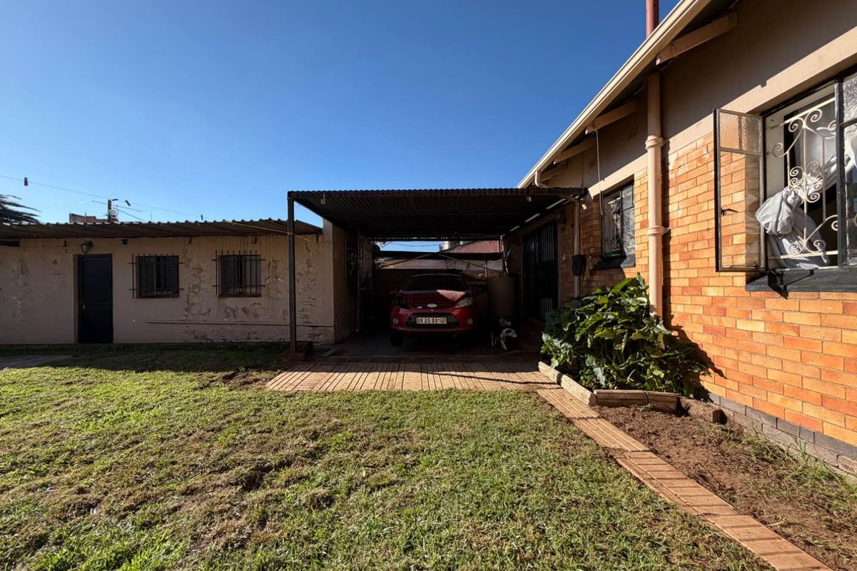 Rear exterior view of the property featuring a brick facade, a covered carport area, and a lawn space.