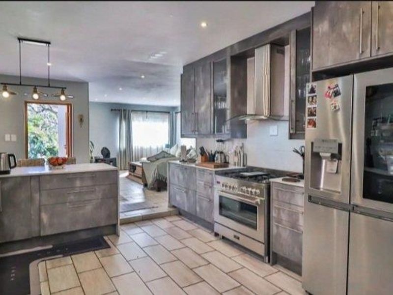 Modern open-plan kitchen featuring sleek grey cabinetry, stone countertops, stainless steel appliances, and tiled flooring, seamlessly flowing into the adjacent living area.