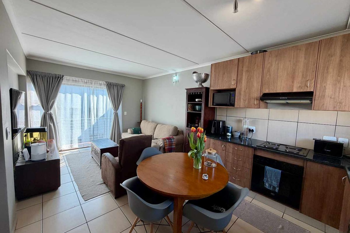 Open-plan living area featuring a functional kitchen with wood-finish cabinetry, granite countertops, and direct access to a balcony through sliding glass doors.