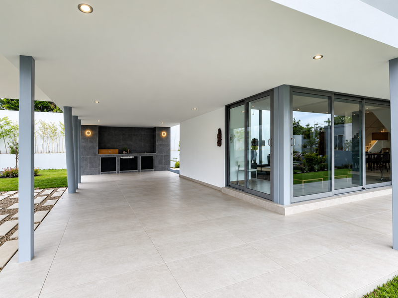 Spacious covered patio featuring large format floor tiles, recessed lighting, and a built-in braai area, seamlessly connecting to the interior through sliding glass doors.