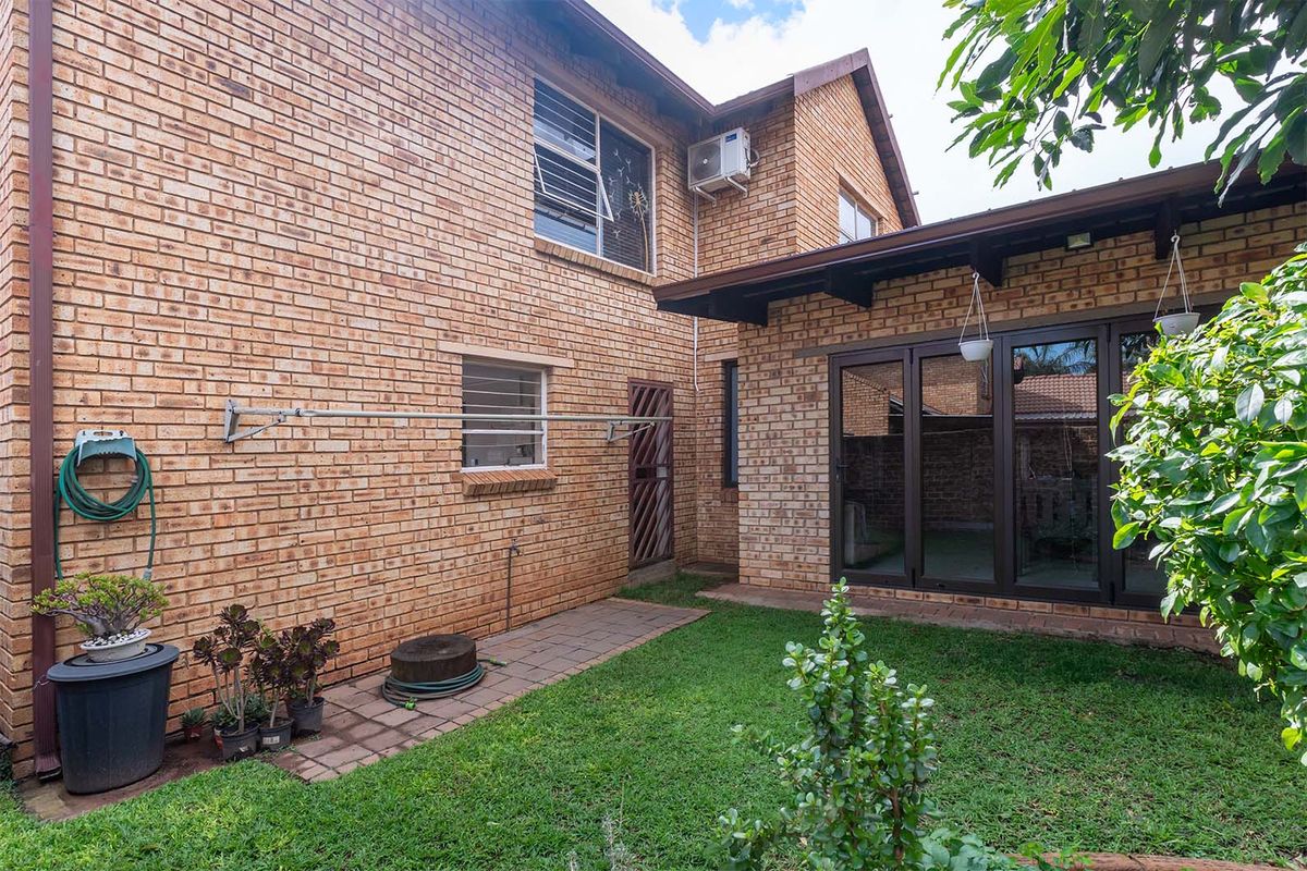 Rear view of the townhouse featuring face-brick exterior, a small private garden, paved walkway, and a covered patio area with dark-framed glass doors.