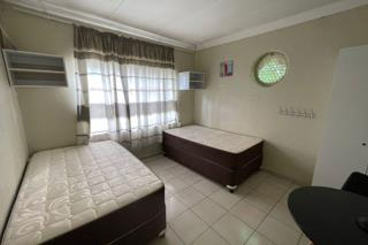 A functional bedroom featuring tiled flooring, built-in wall shelving, and a unique circular window, providing a practical and well-lit living space.