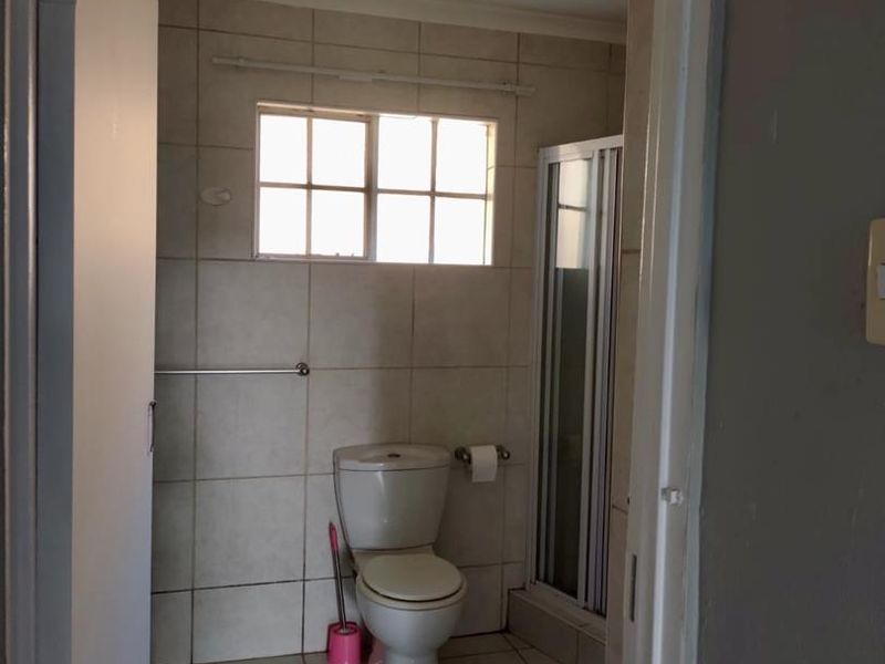 A functional bathroom featuring tiled walls and flooring, a standard toilet, and a shower enclosure with a window for natural light.