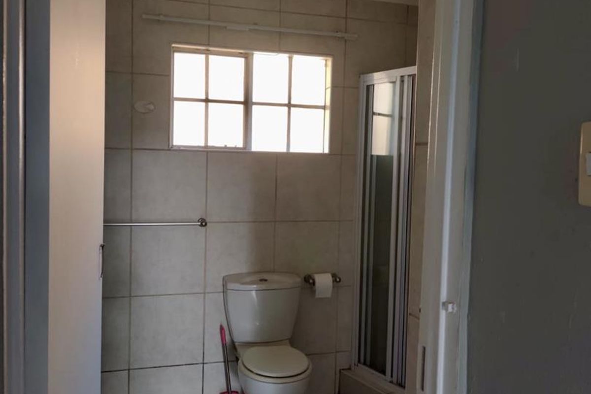 A functional bathroom featuring tiled walls and flooring, a standard toilet, and a shower enclosure with a window for natural light.