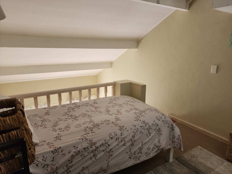 A loft-style bedroom featuring a sloped ceiling, timber balustrade overlooking the lower level, and carpeted flooring.