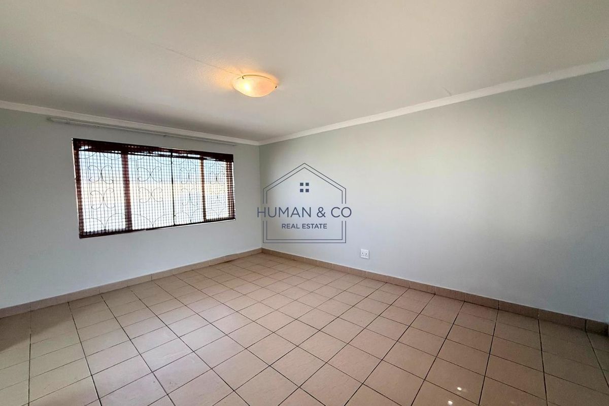 A clean, empty bedroom featuring neutral tiled flooring, a flush-mount ceiling light, and a window fitted with security bars and blinds.