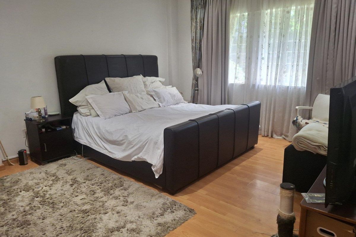 A spacious bedroom featuring laminate flooring and large windows with installed curtain tracks, providing a comfortable and functional living space.
