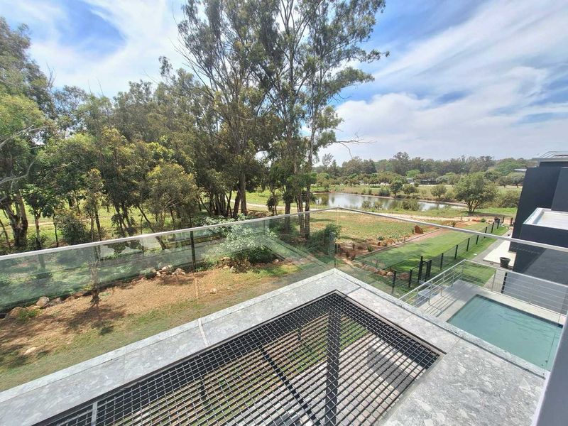 Modern elevated balcony featuring a sleek glass balustrade, stone flooring, and a direct view overlooking the swimming pool and landscaped garden area.